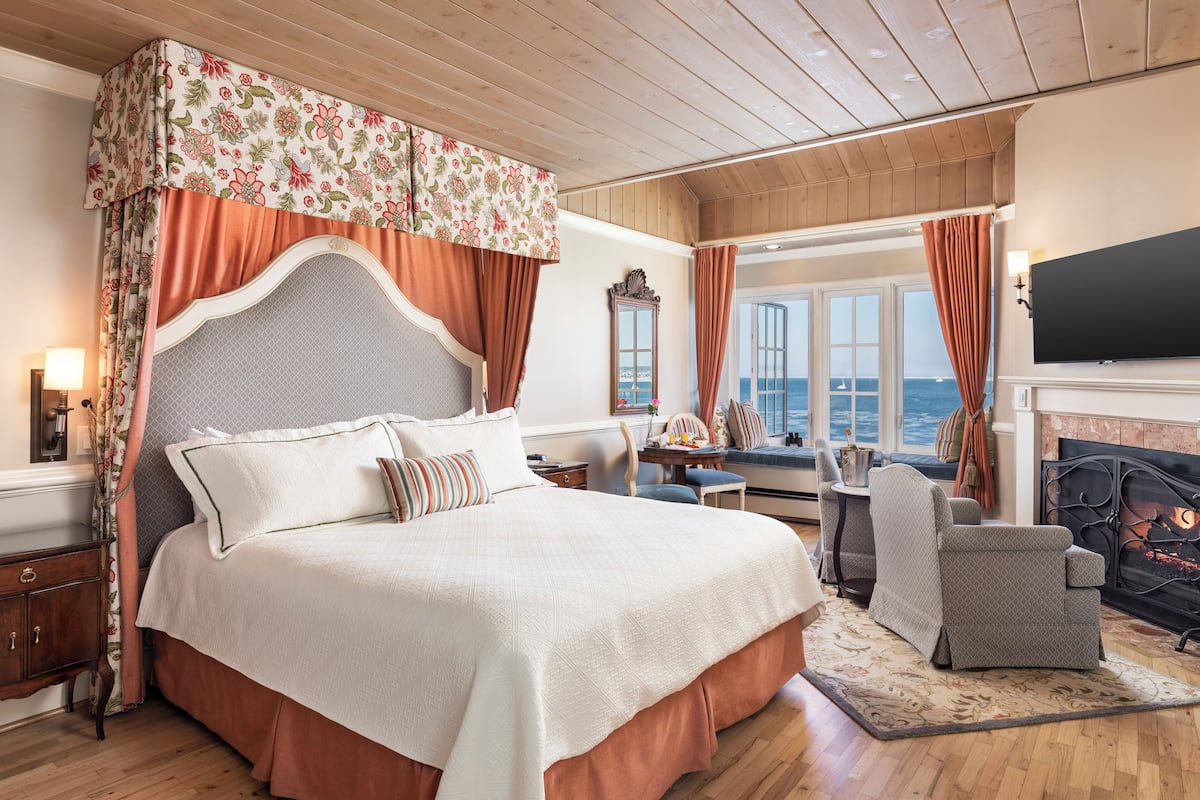 Un dormitorio amplio con una cama grande, una chimenea, vistas al mar y una zona de estar acogedora.