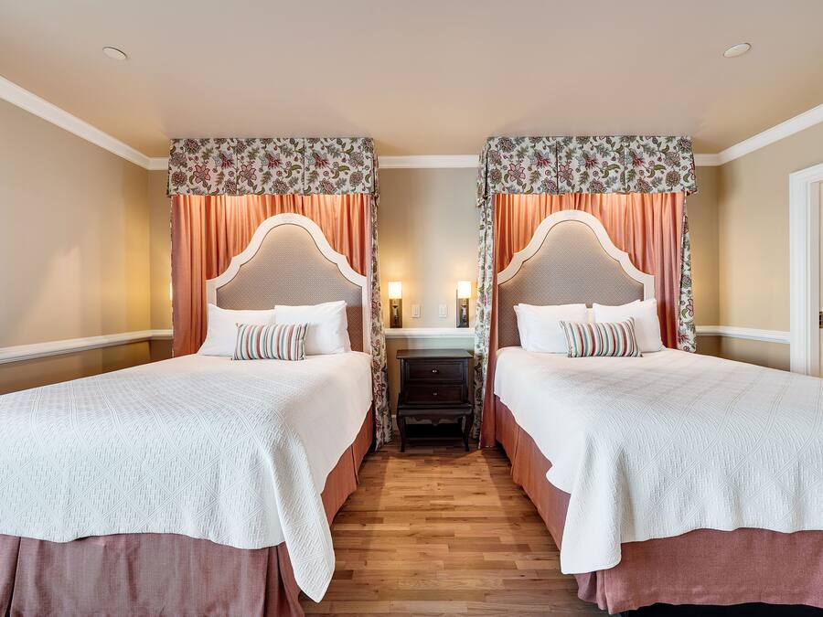 A hotel room with two beds, each with a canopy and a nightstand.