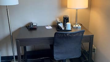 Ein Hotelzimmer mit Schreibtisch, Stuhl, Lampe, Telefon und Kaffeemaschine.