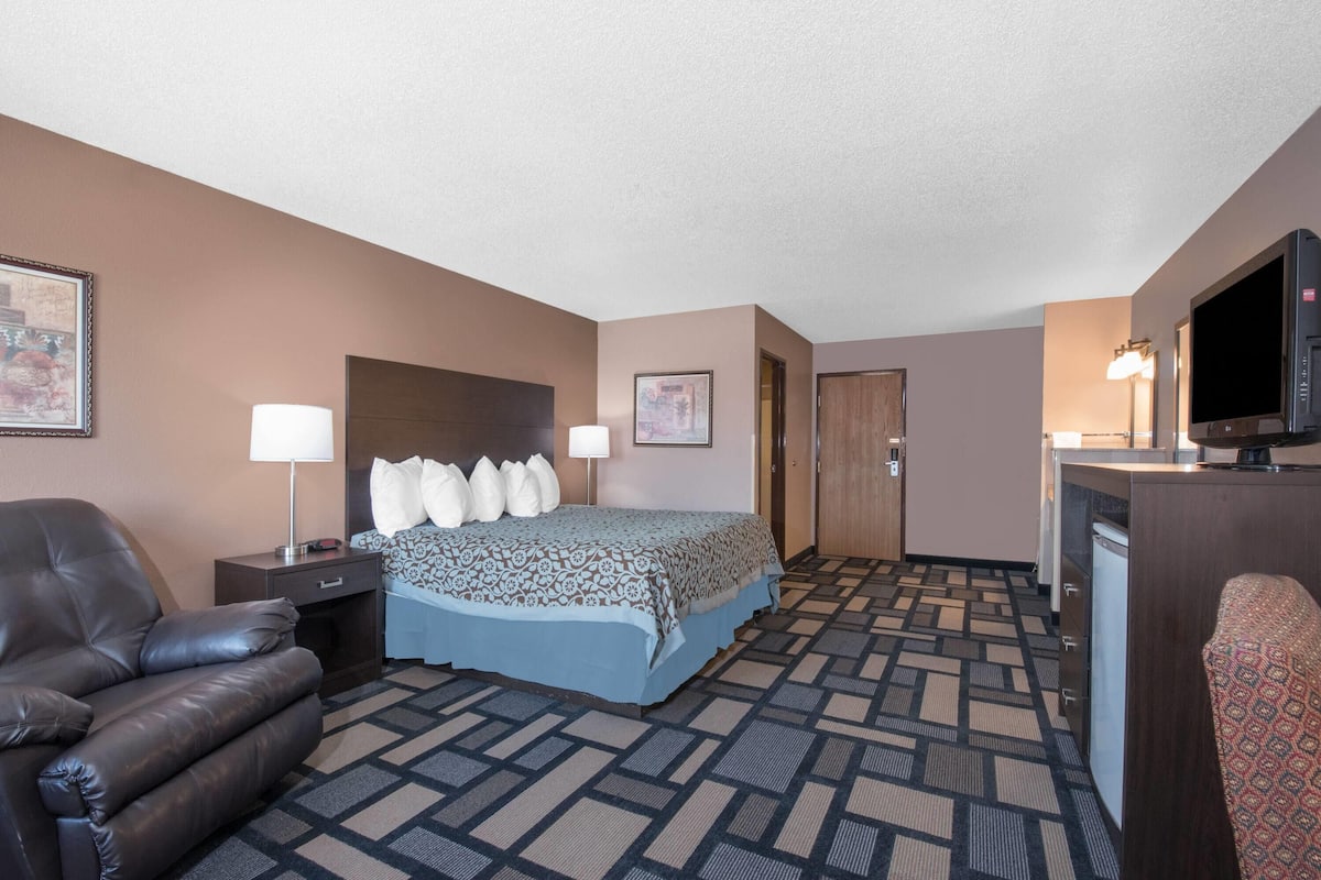 A hotel room with a bed, a desk, a chair, a television, and a door.