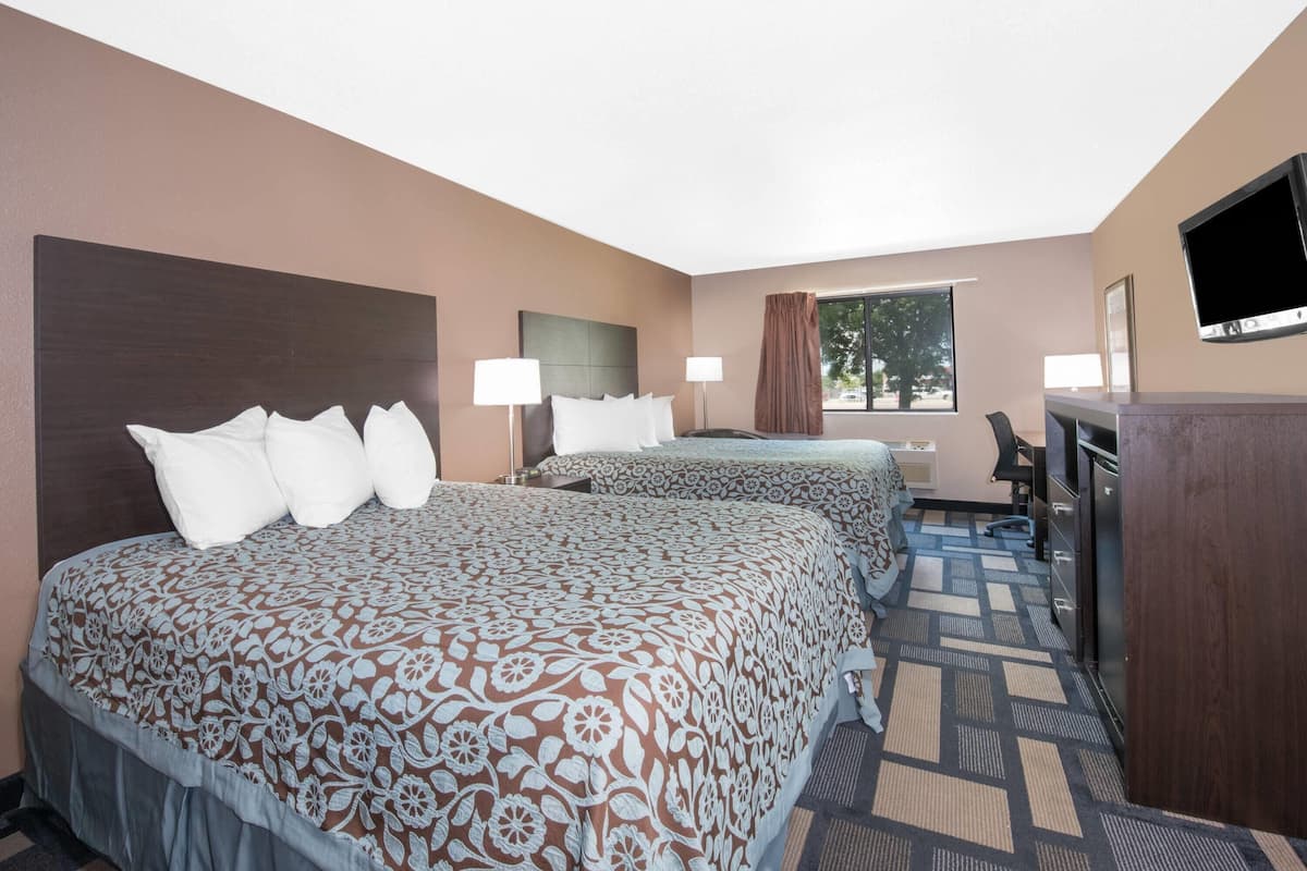 A hotel room with two beds, a desk, a chair, a TV, and a window with curtains.