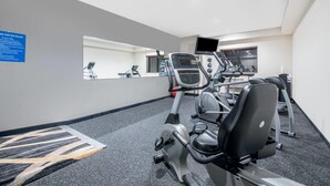 Une salle de sport équipée d’appareils de cardio, d’un miroir et d’un panneau affichant les règles.