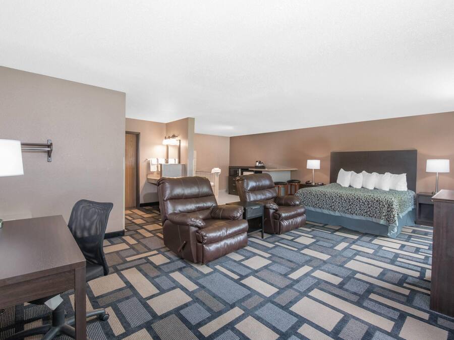 A hotel room with a bed, two recliners, a desk, and a television.