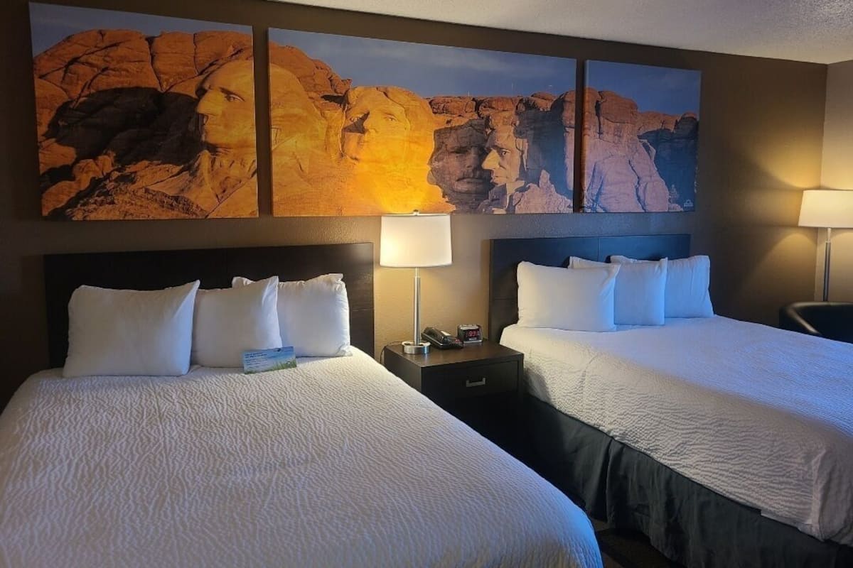 A hotel room with two beds, a nightstand with a lamp, and a large painting on the wall.