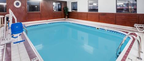 Una piscina interior con paneles de madera, una silla de salvavidas y vistas de la ciudad a través de amplias ventanas.