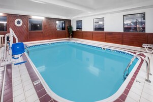 Una piscina interior con paneles de madera, una silla de salvavidas y vistas de la ciudad a través de amplias ventanas.