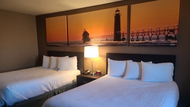Une chambre d’hôtel avec deux lits, une table de chevet avec une lampe et un grand tableau représentant un phare et une jetée, accroché au mur.
