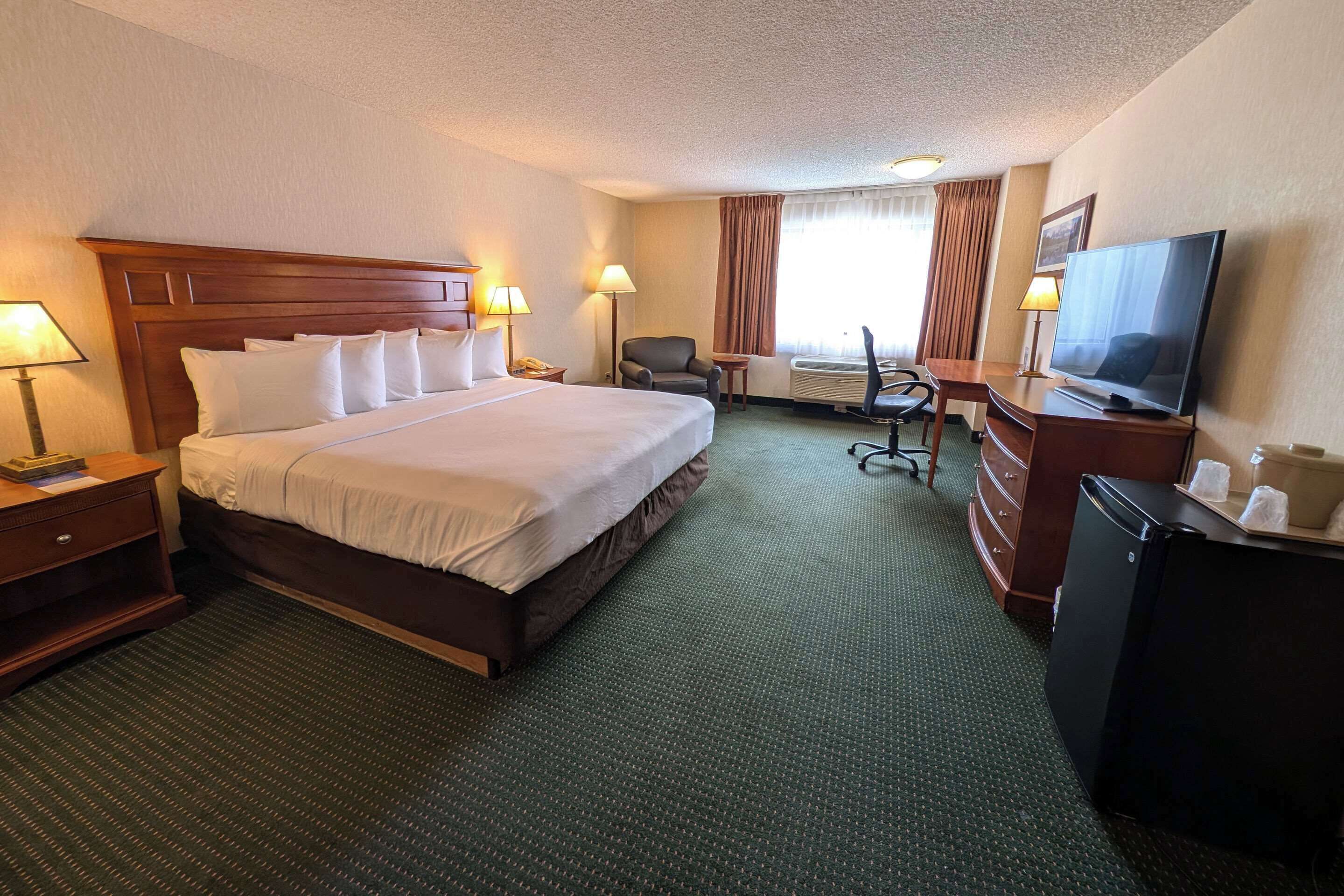A hotel room with a large bed, a desk with a television, a chair, and a small table.
