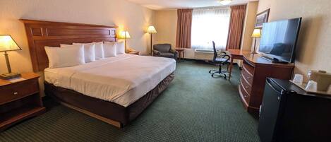 A hotel room with a large bed, a desk with a television, a chair, and a small table.