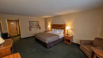 Une chambre d’hôtel avec un grand lit, deux tables de chevet avec des lampes, une tête de lit en bois, un petit canapé et un bureau.