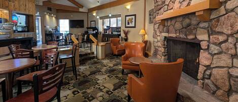 A cozy restaurant with wooden beams, stone walls, and a fireplace. Tables and chairs are arranged for dining.