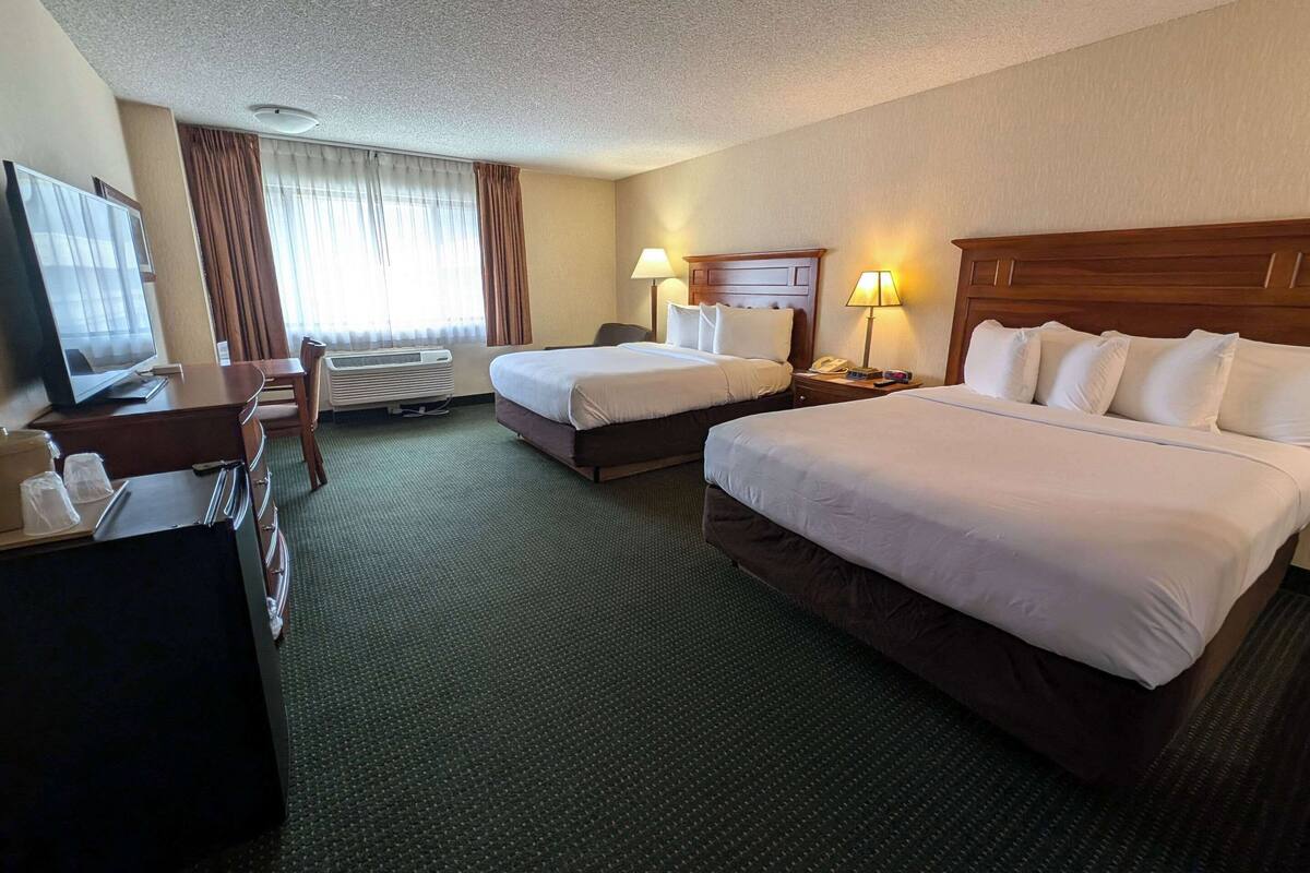 A hotel room with two beds, a desk with a TV, a chair, and a desk lamp.