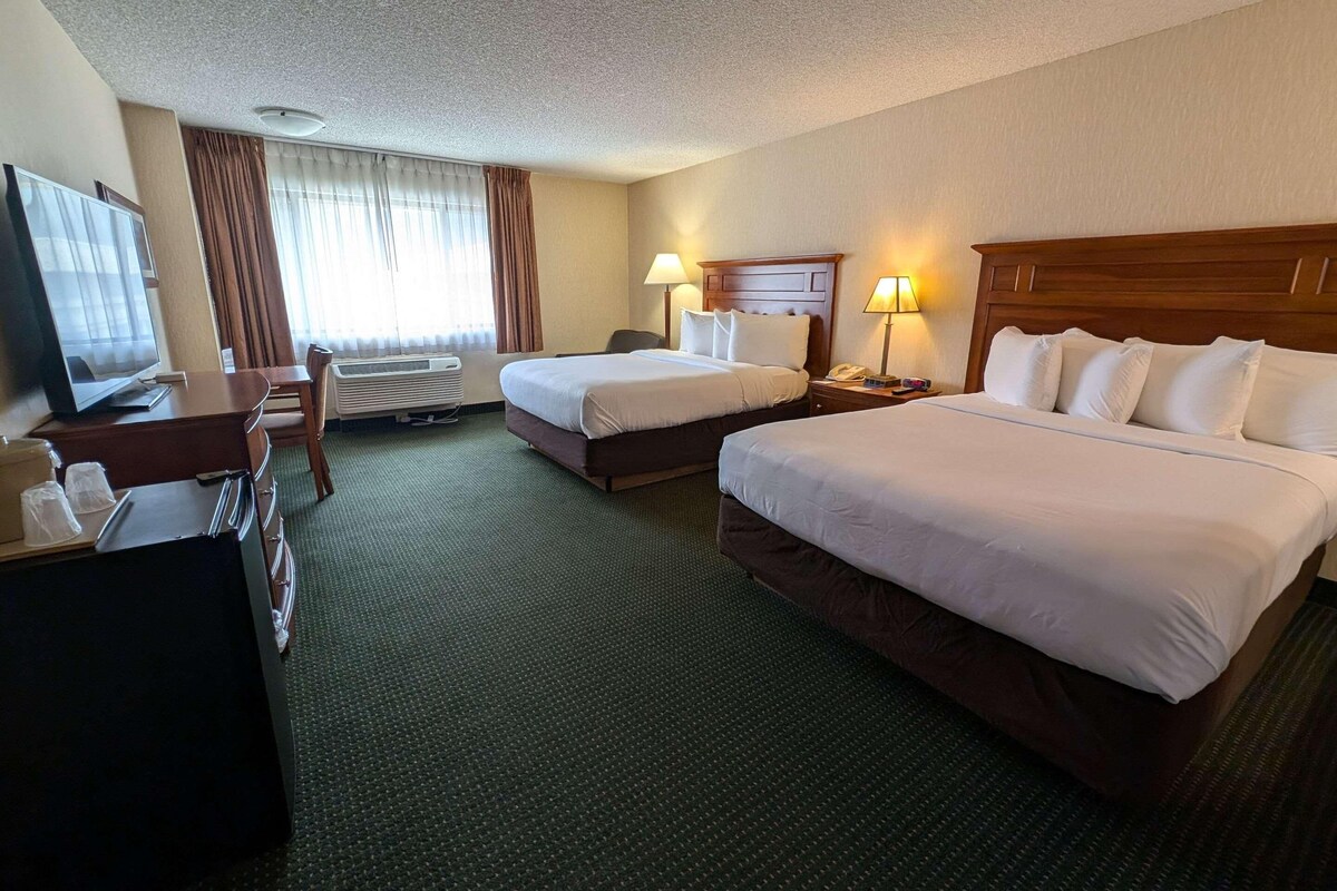 A hotel room with two beds, a desk with a TV, a chair, and a desk lamp.