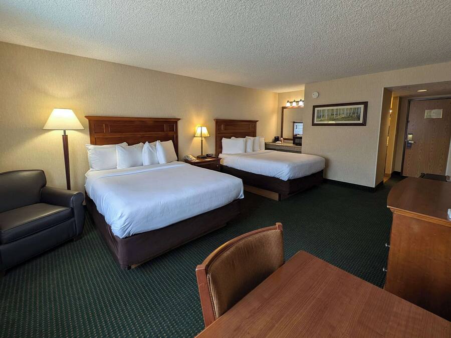 A hotel room with two beds, a desk, a chair, a sofa, and a lamp.