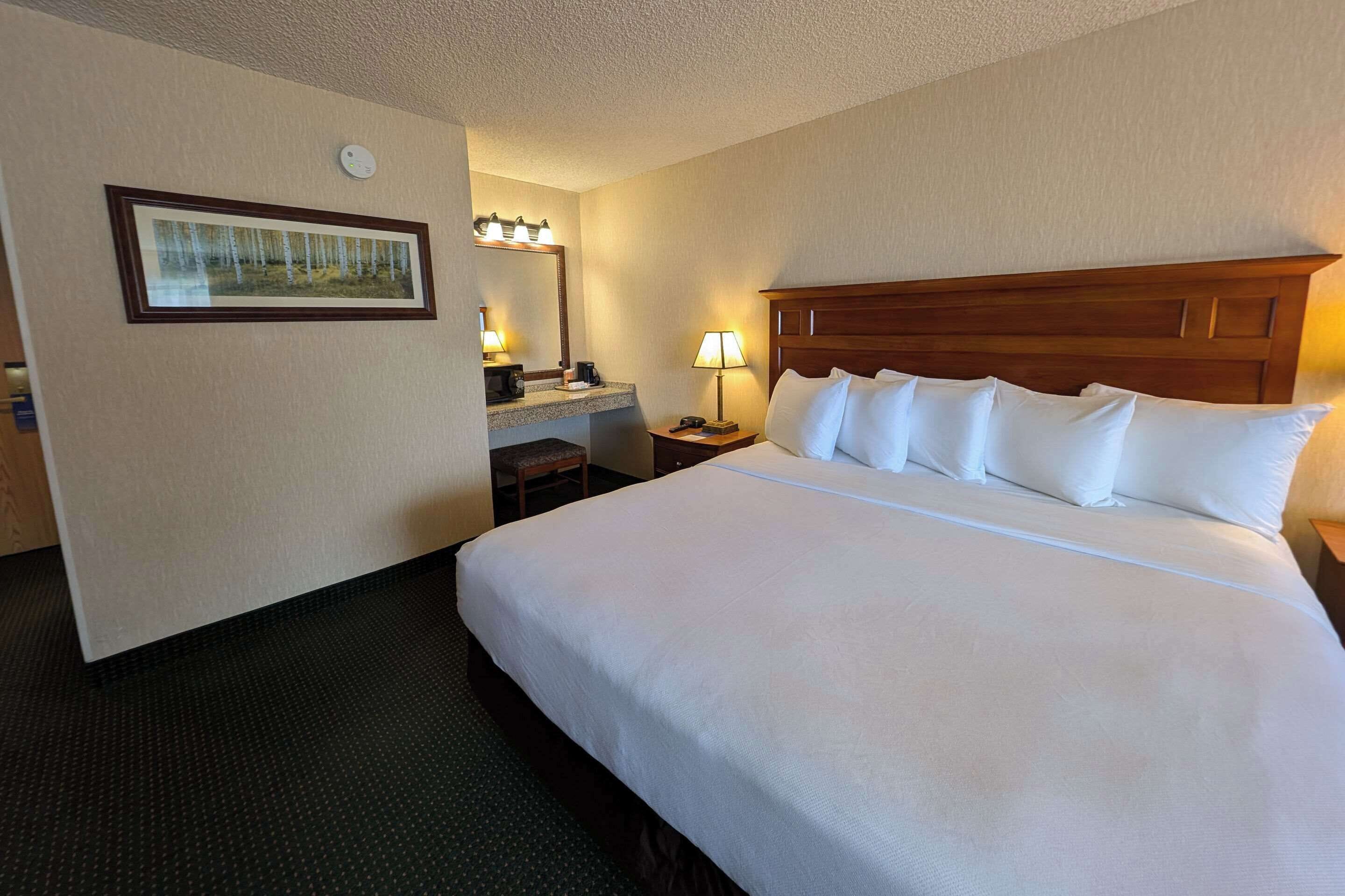 A hotel room with a large bed, a desk with a lamp, a framed picture on the wall, and a ceiling light.