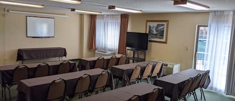 A conference room with multiple tables and chairs, a projector screen, a television, and an air conditioning unit.