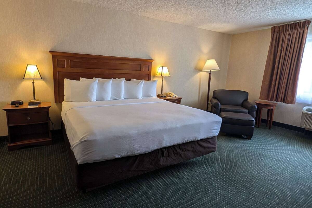 A hotel room with a large bed, two bedside tables with lamps, a chair, and a small table.