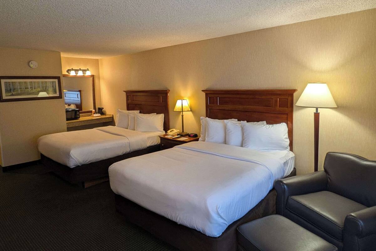 A hotel room with two beds, a desk, a chair, and a lamp.