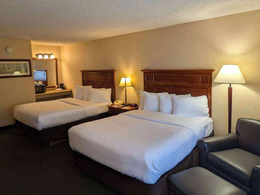 Quarto de hotel com duas camas, uma escrivaninha, uma cadeira e um abajur.
