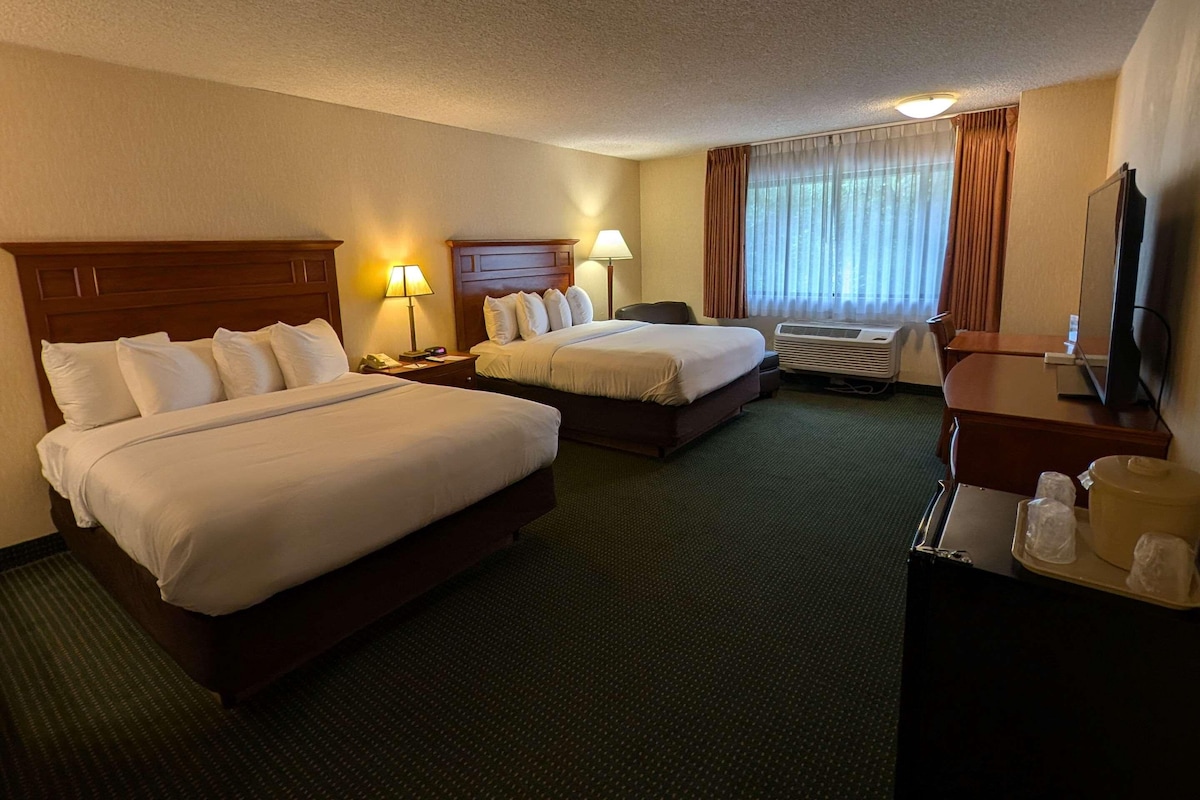 A hotel room with two beds, a desk, a television, and an air conditioning unit.