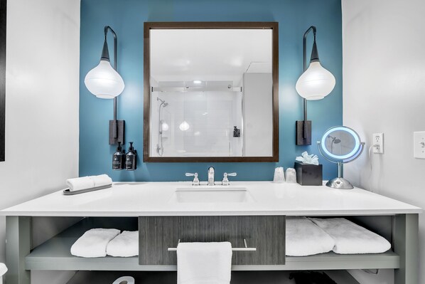 A modern bathroom with a large mirror, two wall-mounted lights, a sink, and a vanity with a towel rack. - Hotel Indigo Atlanta-Vinings Ballpark Area by IHG (Atlanta)