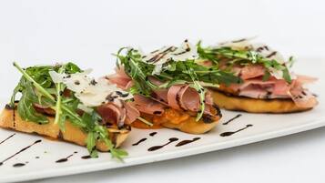 A plate with two pieces of toast topped with greens, prosciutto, and shaved cheese, with a drizzle of sauce.