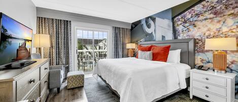 A modern hotel room with a large bed, a desk with a computer, and a view of the outdoors.