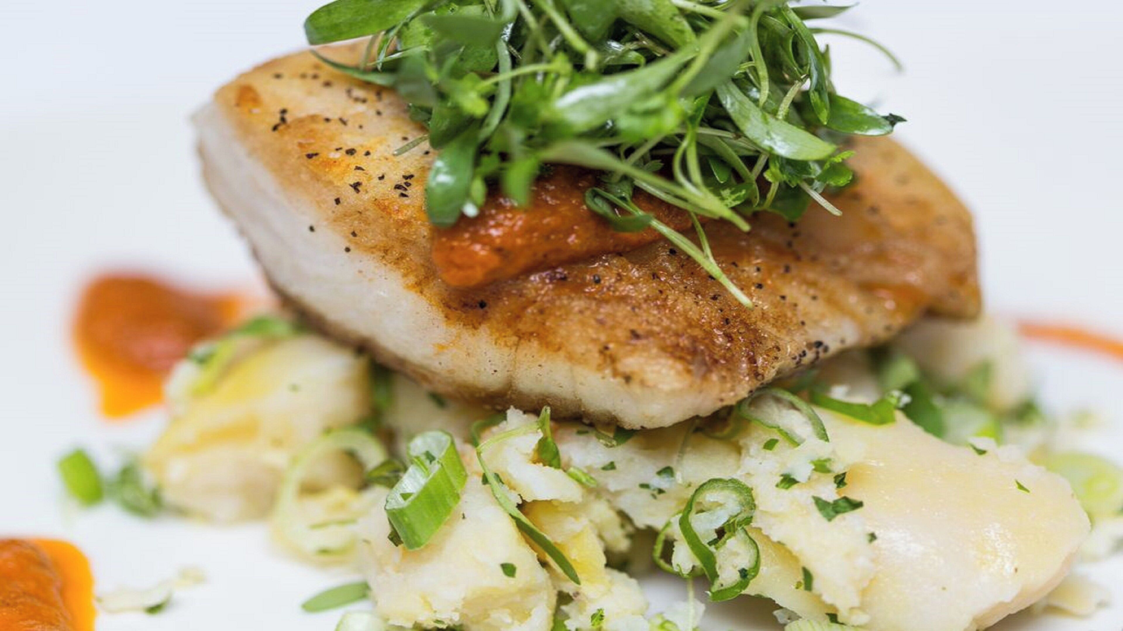 A dish with a seared fish topped with greens and a side of mashed potatoes.