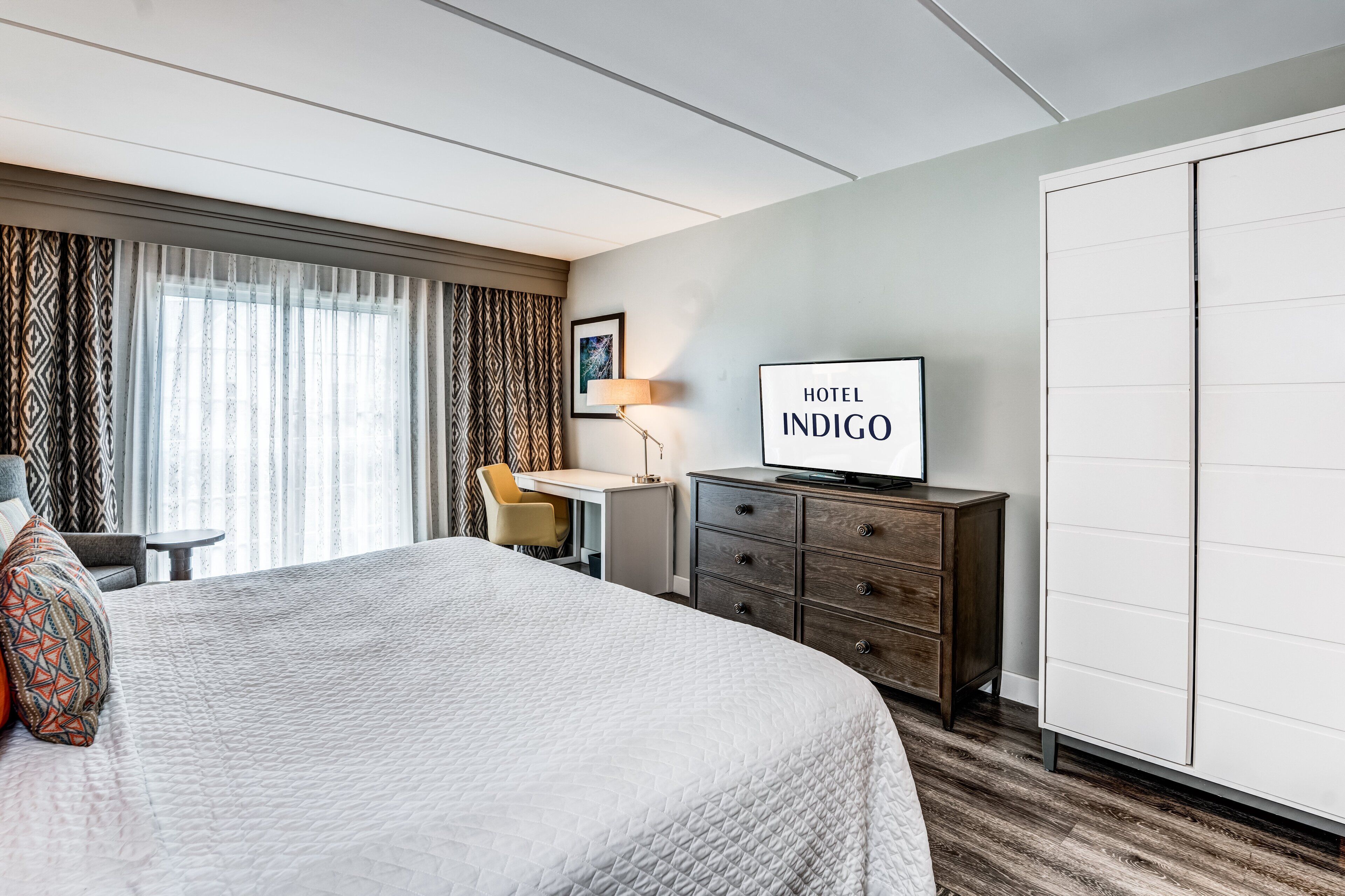A hotel room with a large bed, a desk, a chair, a dresser, and a wardrobe.