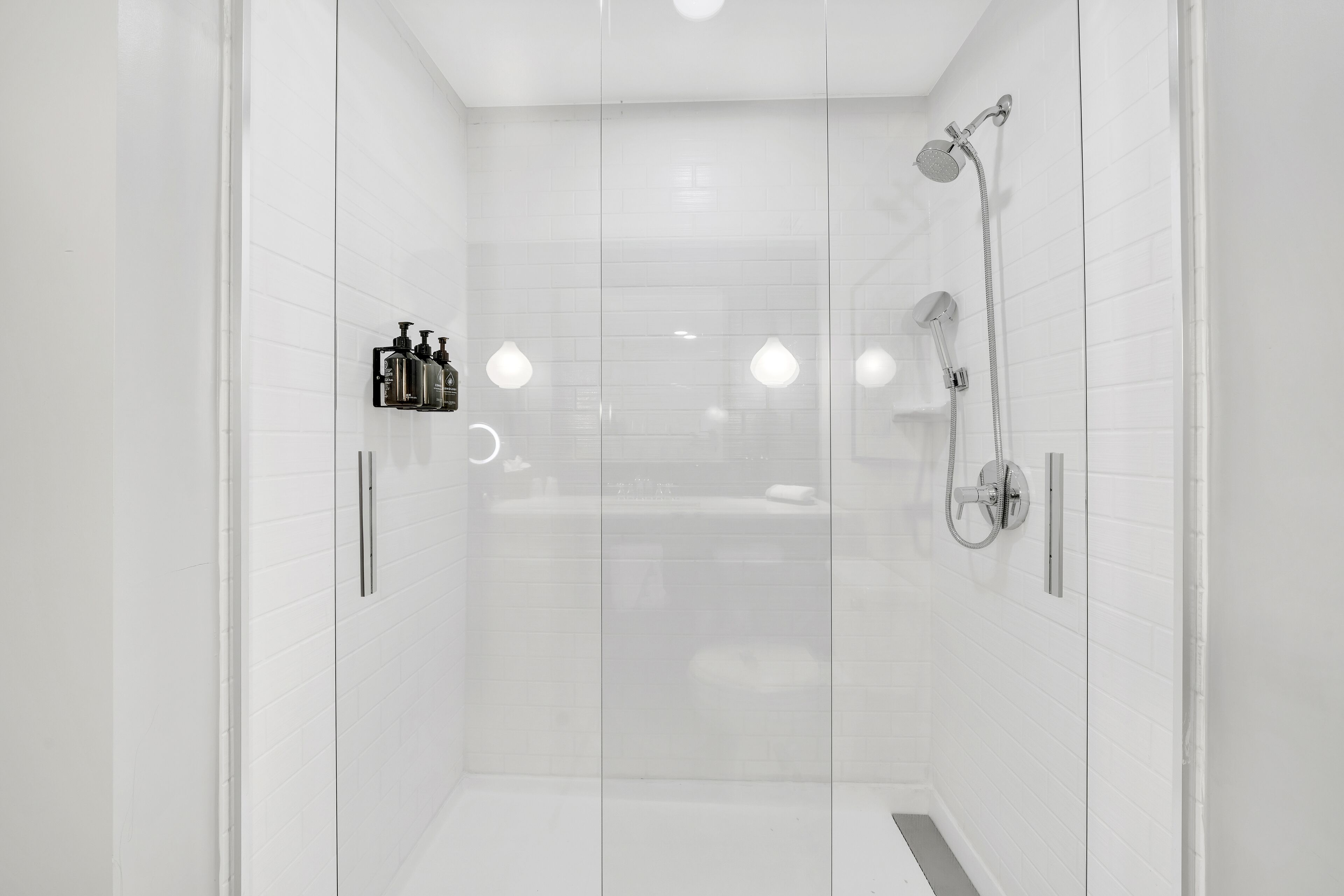 Une douche moderne dotée d’une porte en verre, d’un pommeau de douche à main et d’un robinet mural.