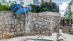 A stone wall with a water feature, a pool, and a metal staircase. - Hotel Indigo Atlanta-Vinings Ballpark Area by IHG (Atlanta)