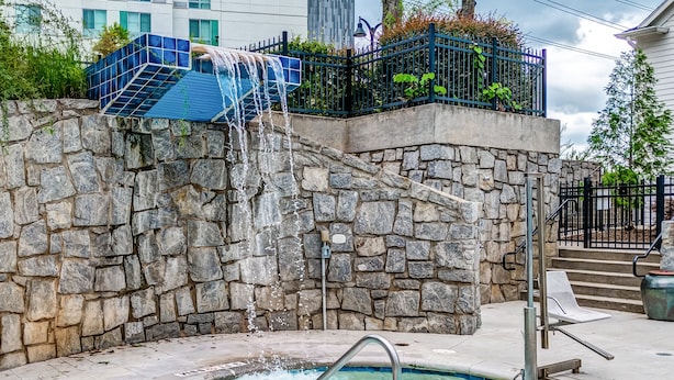A stone wall with a water feature, a pool, and a metal staircase. - Hotel Indigo Atlanta-Vinings Ballpark Area by IHG (Atlanta)