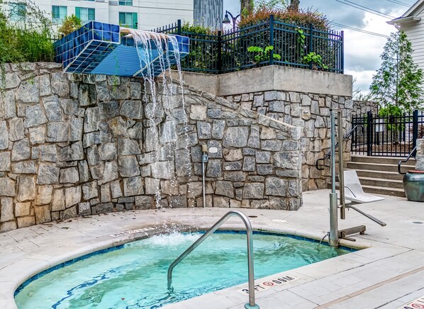 A stone wall with a water feature, a pool, and a metal staircase. - Hotel Indigo Atlanta-Vinings Ballpark Area by IHG (Atlanta)