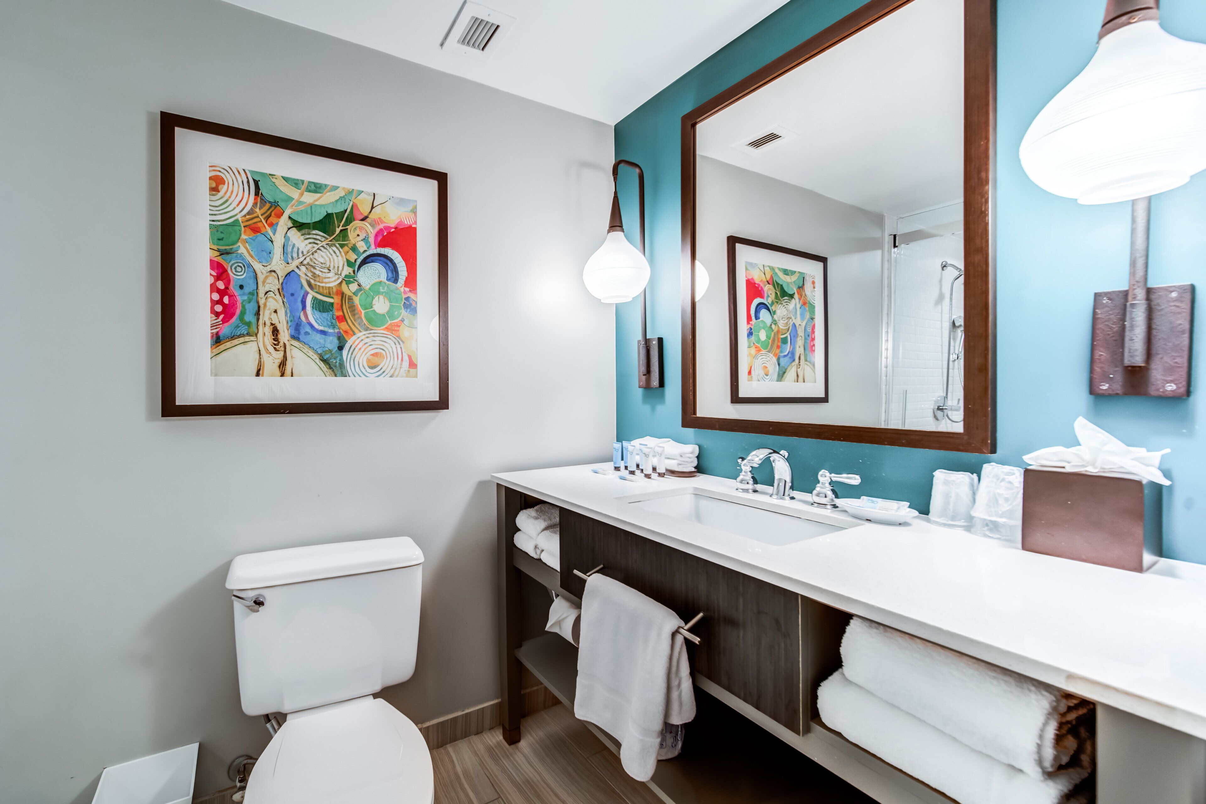 Een moderne badkamer met een wit toilet, een grote spiegel en een witte wastafel. Handdoeken en toiletartikelen liggen op het aanrecht.