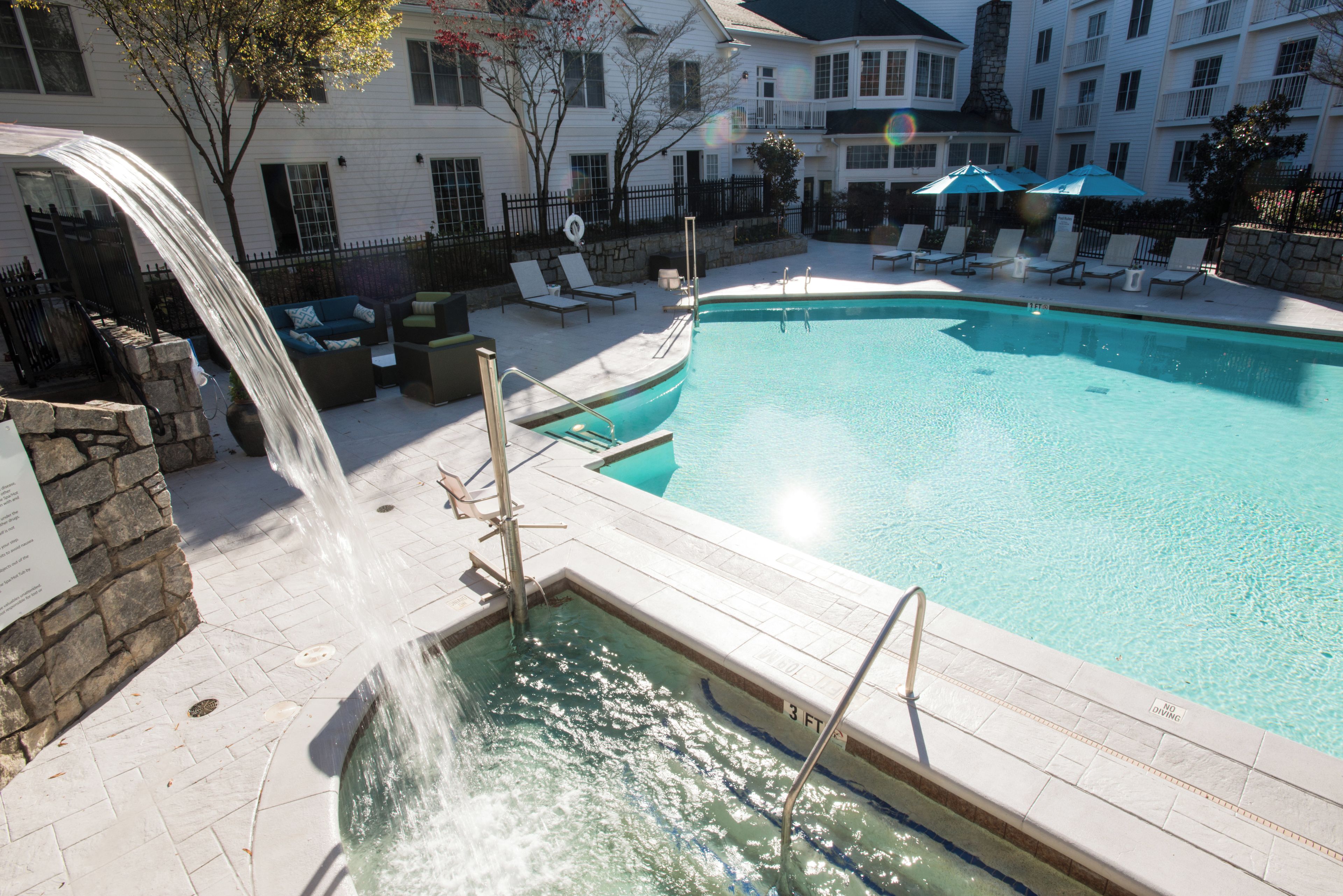 A swimming pool with a waterfall feature, lounge chairs, and a stone wall.