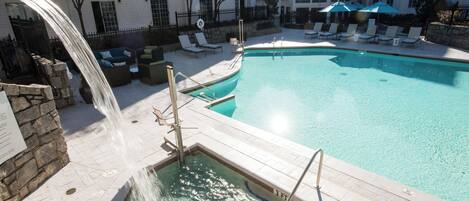 A swimming pool with a waterfall feature, lounge chairs, and a stone wall.