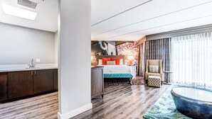 A modern hotel room with a wooden floor, a bed with a green bedspread, a sitting area with a round coffee table, and a view of the city through large windows. - Hotel Indigo Atlanta-Vinings Ballpark Area by IHG (Atlanta)