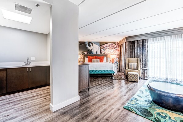 A modern hotel room with a wooden floor, a bed with a green bedspread, a sitting area with a round coffee table, and a view of the city through large windows. - Hotel Indigo Atlanta-Vinings Ballpark Area by IHG (Atlanta)
