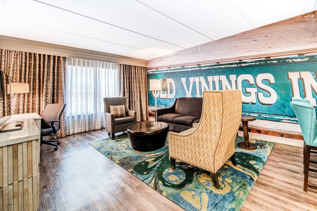 A hotel room with a large window, a sofa, a chair, a coffee table, and a rug.