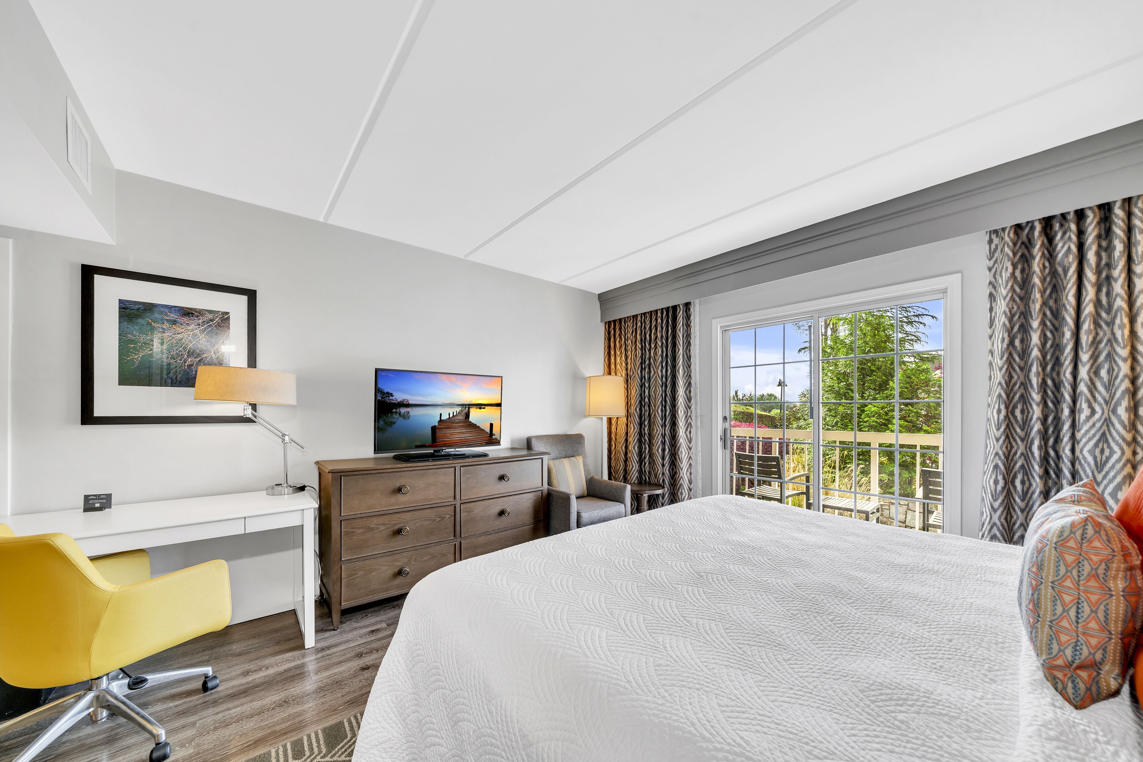 Habitación de hotel con una cama grande, un escritorio con una silla, un televisor y vistas al exterior.