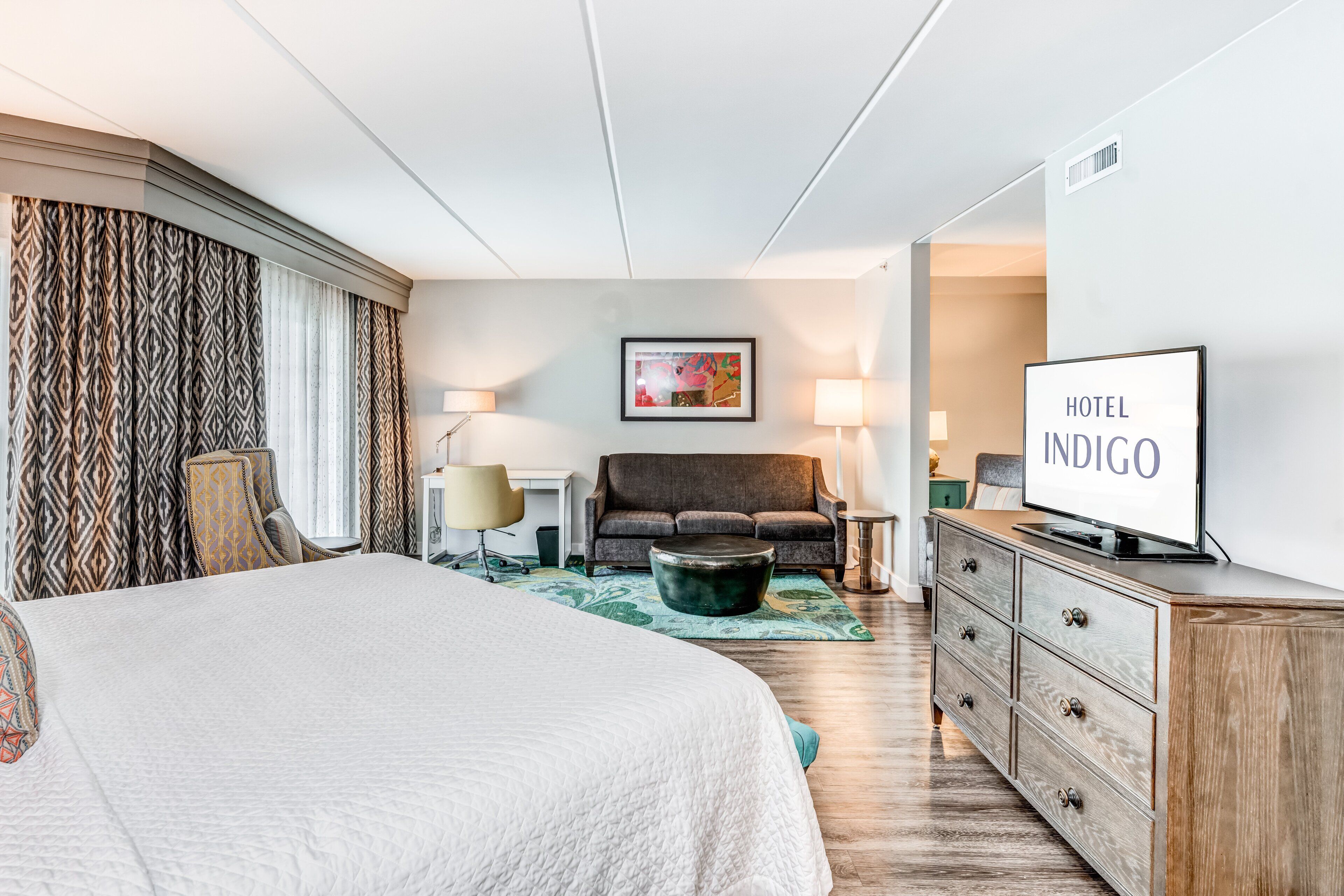 A hotel room with a large bed, a sofa, a TV, and a desk.