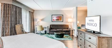A hotel room with a large bed, a sofa, a TV, and a desk.