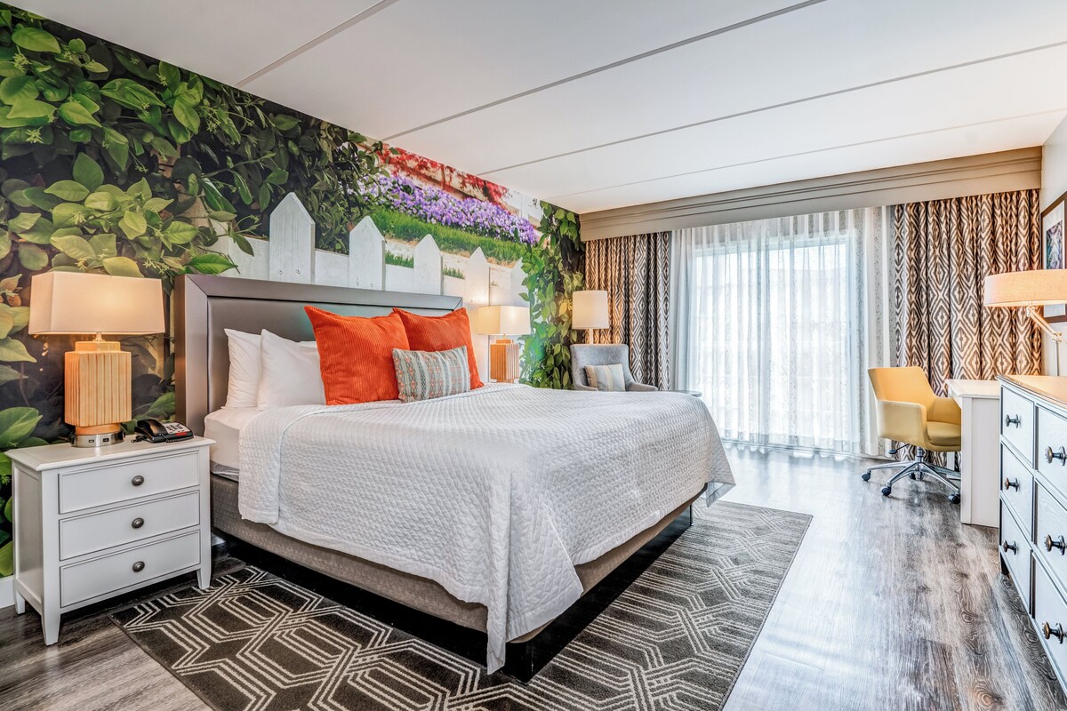 A modern hotel room with a large bed, two bedside tables, a desk, and a chair.