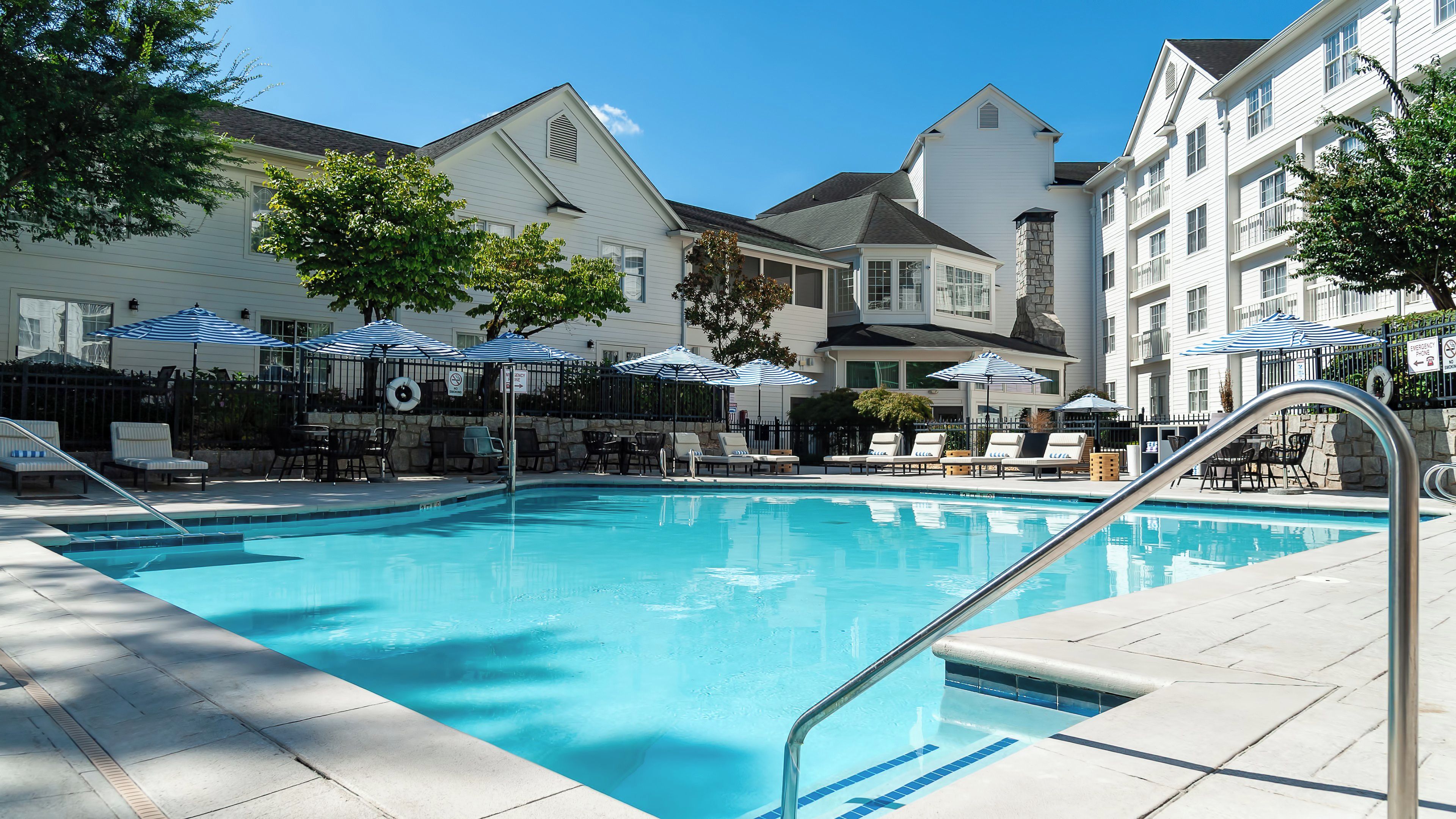 A swimming pool with lounge chairs and umbrellas, surrounded by buildings with a classic architectural style.