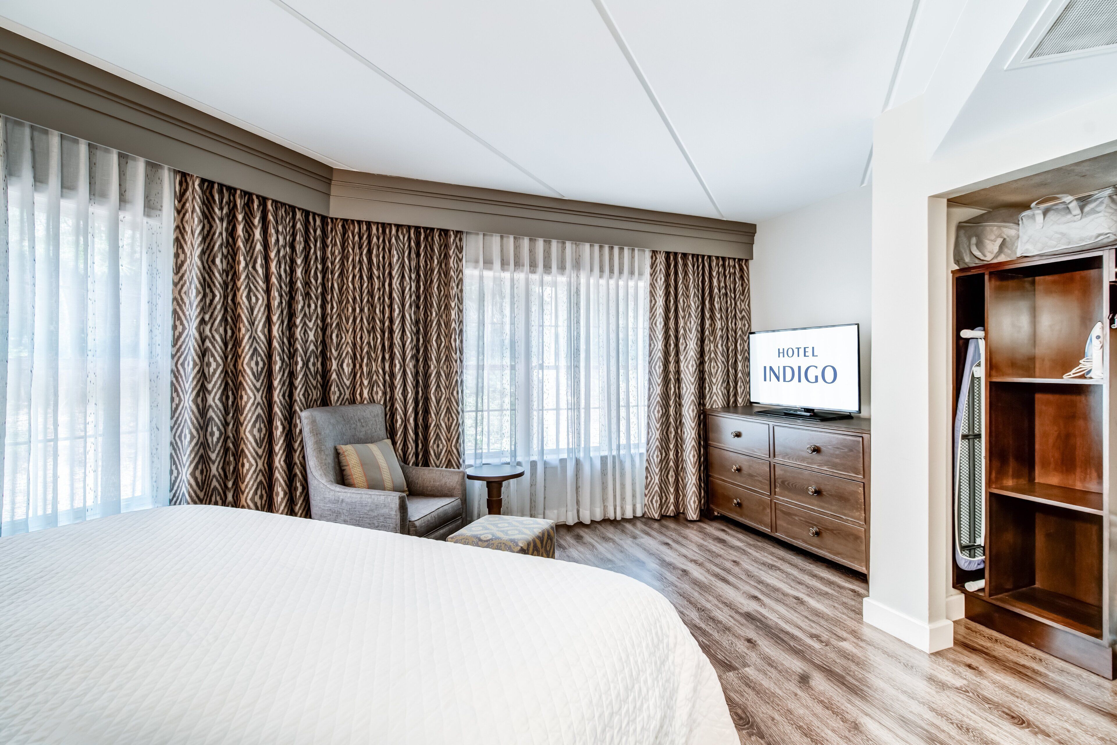 Una habitación de hotel con una cama grande, una silla, una mesita, un televisor y un armario.