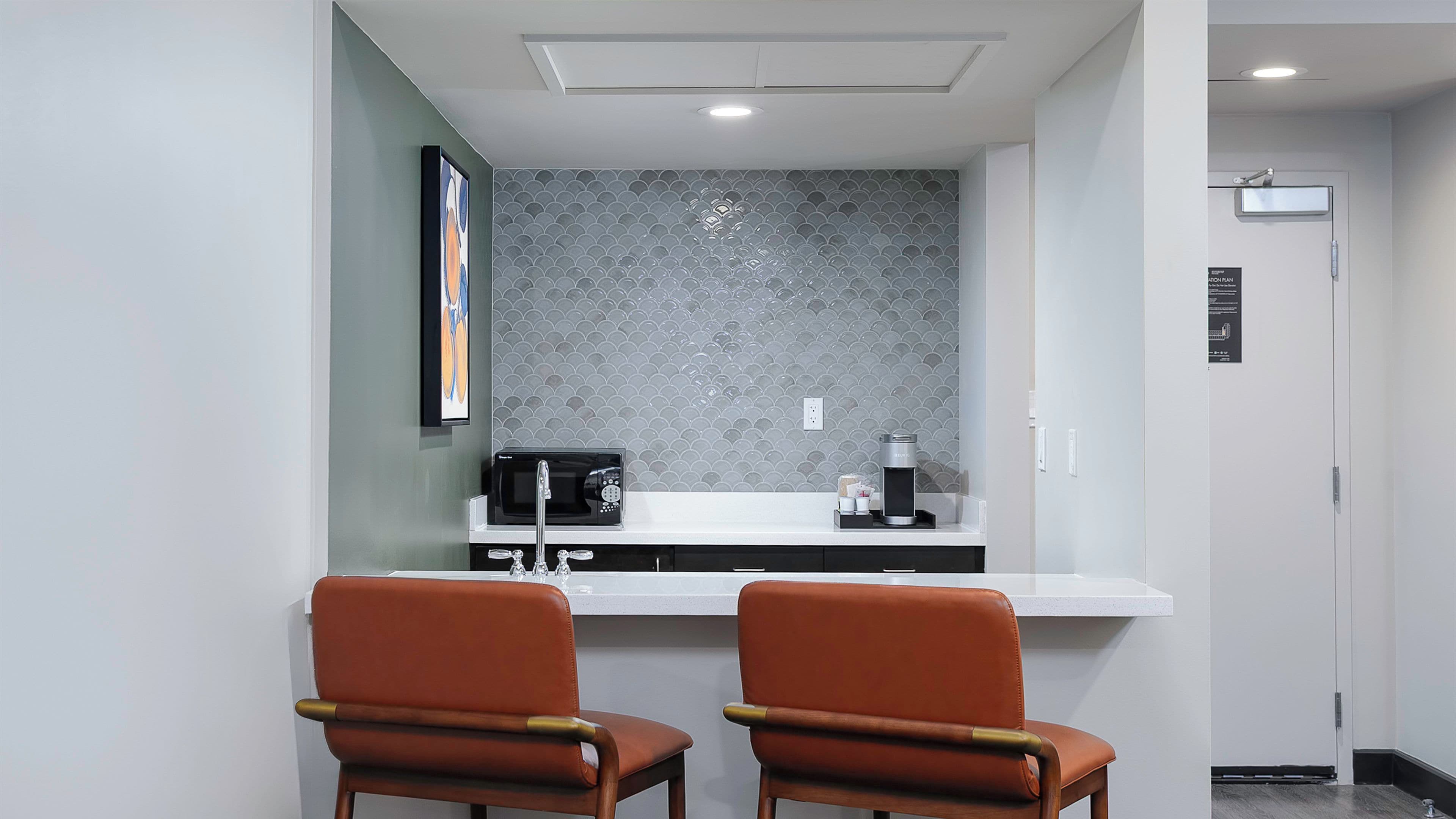 A modern kitchen area with a countertop, two chairs, a coffee machine, and a microwave.