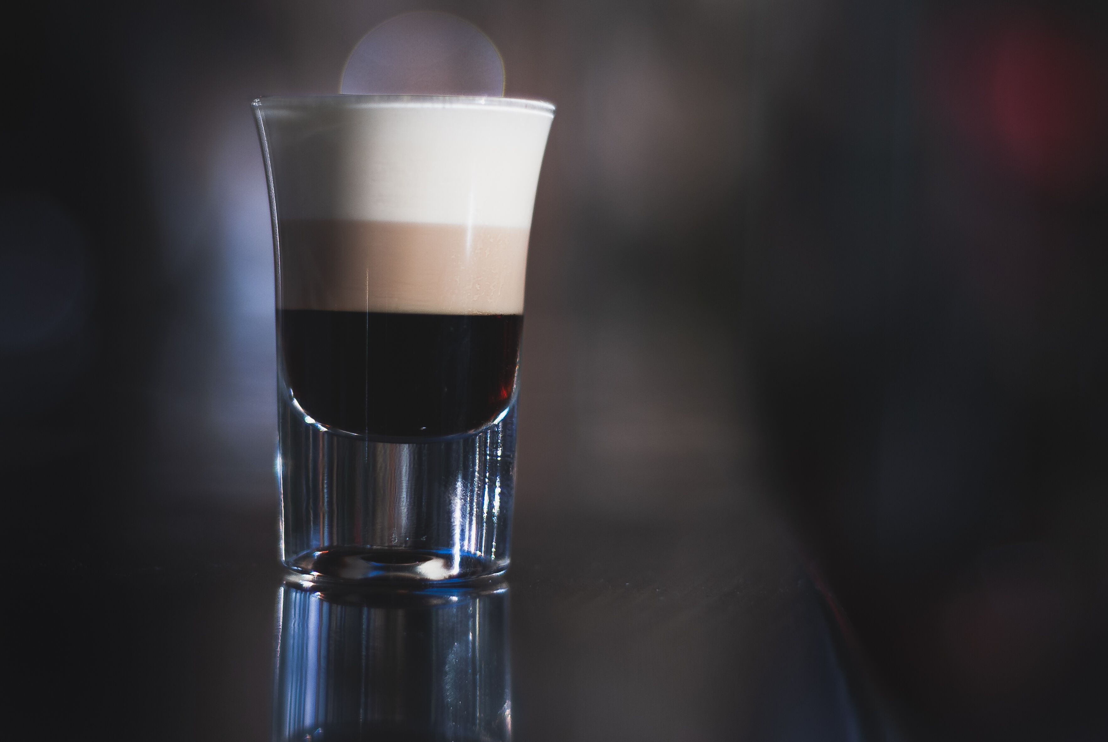 A clear glass with a layered beverage, reflecting on a surface.