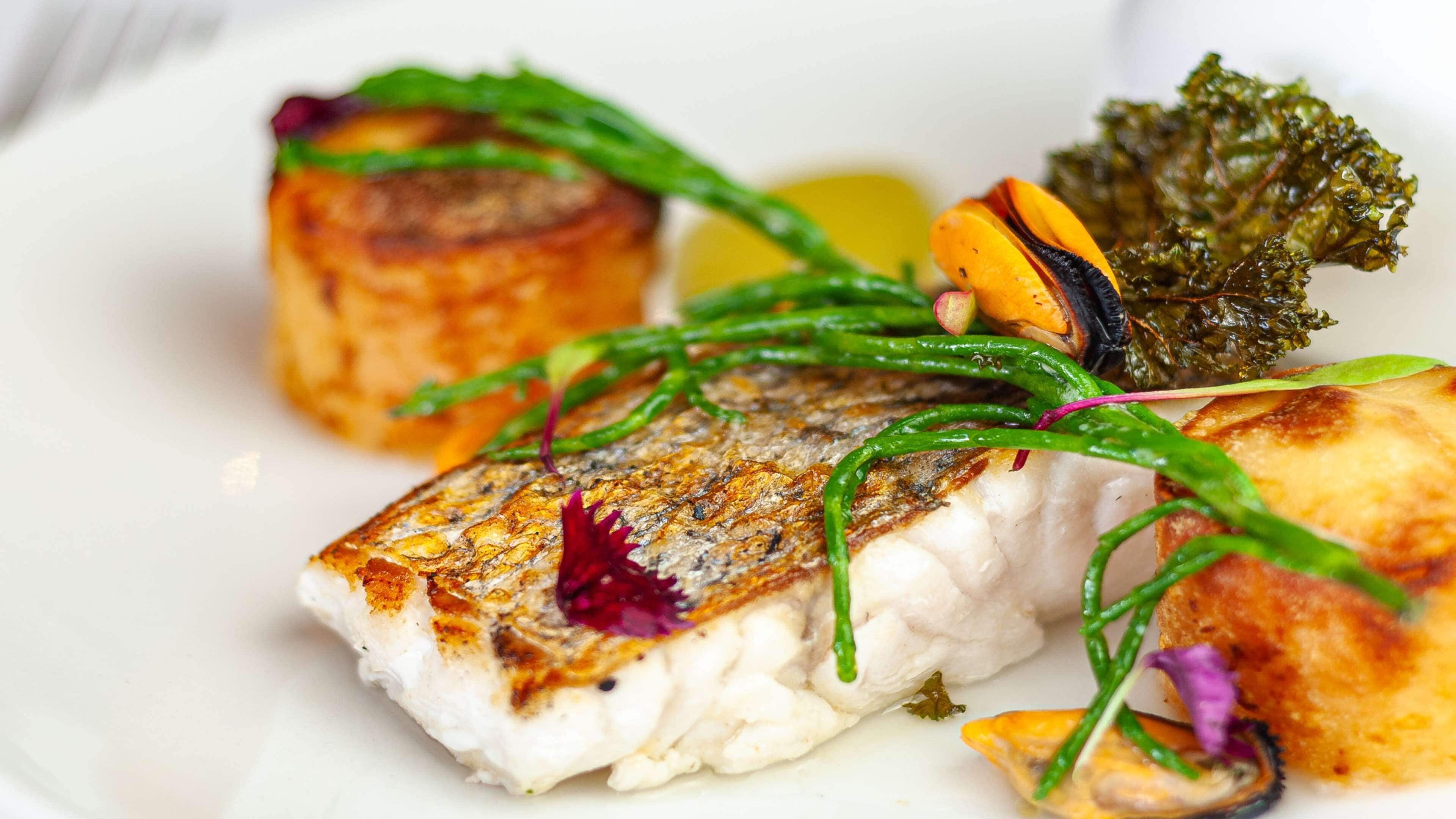 Une assiette contenant un poisson grillé, des légumes verts et un morceau qui ressemble à une pomme de terre.