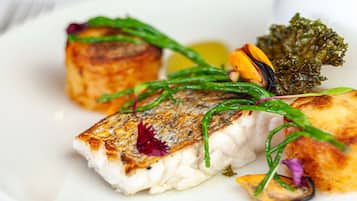 Une assiette contenant un poisson grillé, des légumes verts et un morceau qui ressemble à une pomme de terre.