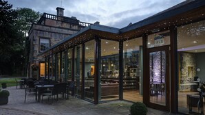 An outdoor seating area with tables and chairs, a stone building in the background, and string lights above the entrance. - Mosborough Hall Hotel, BW Signature Collection (Sheffield)